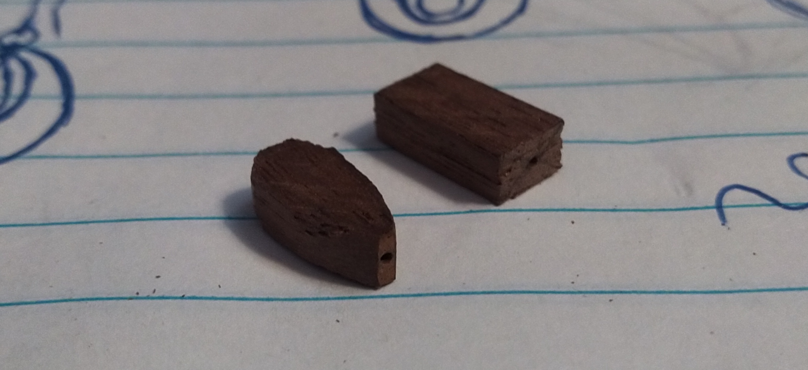 Two very small pieces of walnut wood. One is rectangular and the other has been rounded to a teardrop shape.