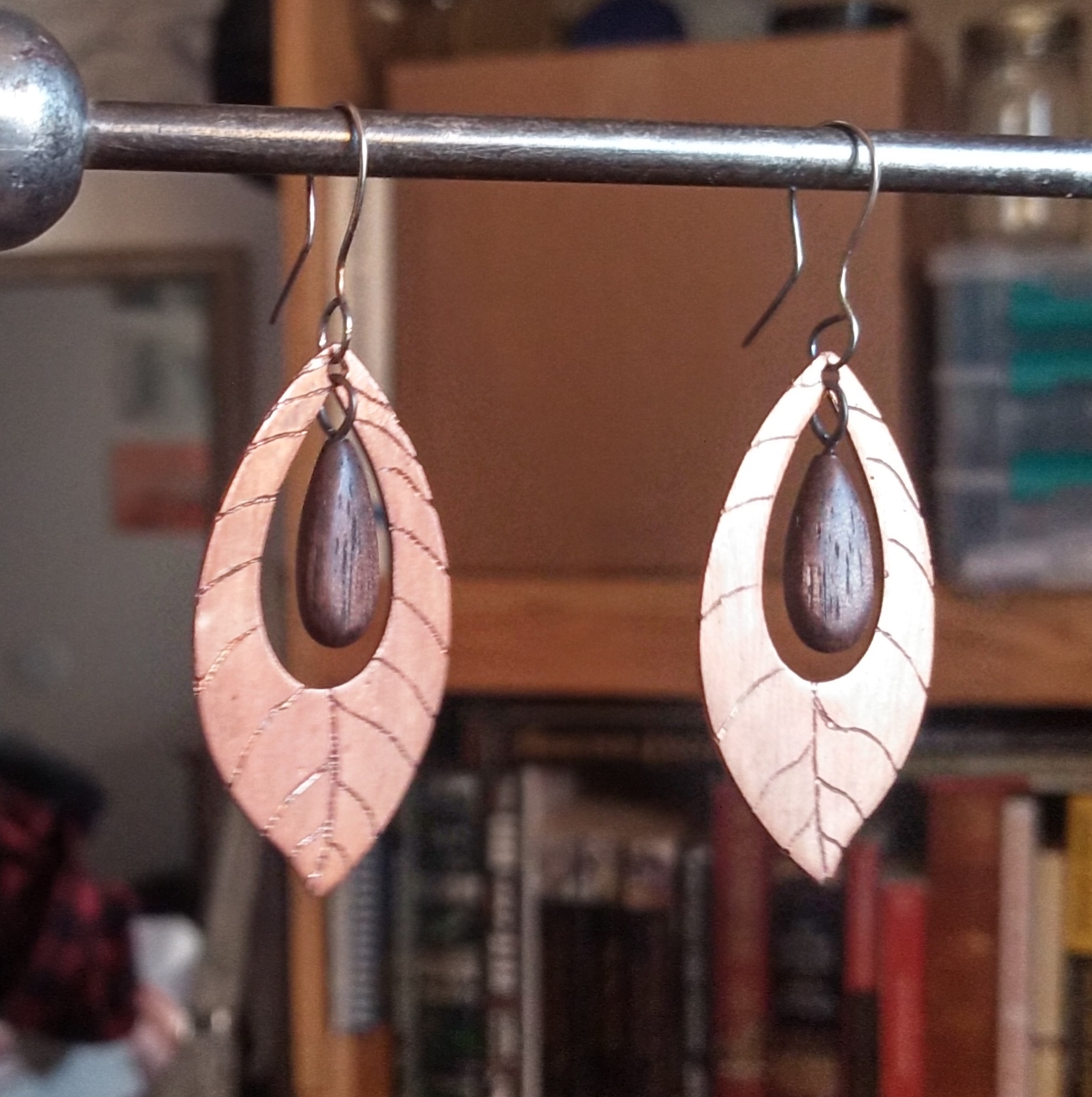 Two copper earrings shaped like walnut leaves with walnut wood pendants within them