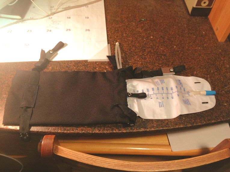 A black pouch with straps and buckles containing a foley catheter bag