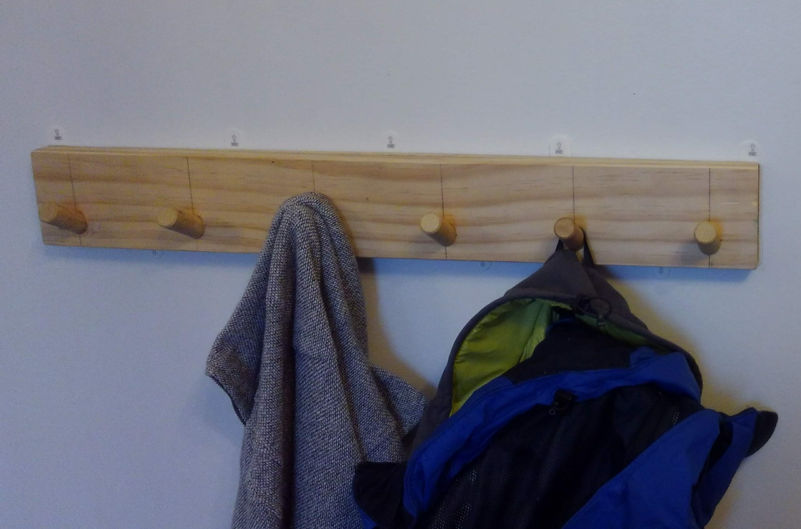 a wooden panel with six coat hooks adhered to the wall