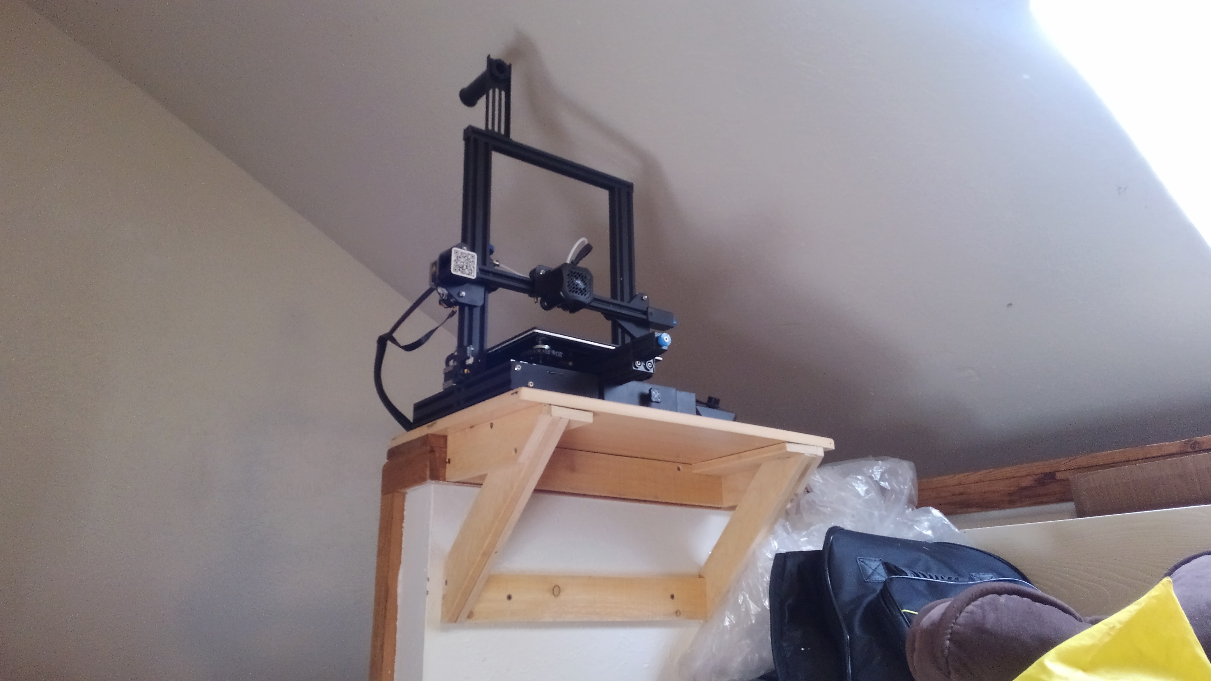A triangle frame shelf holding a 3D printer. It is attached to a low wall.