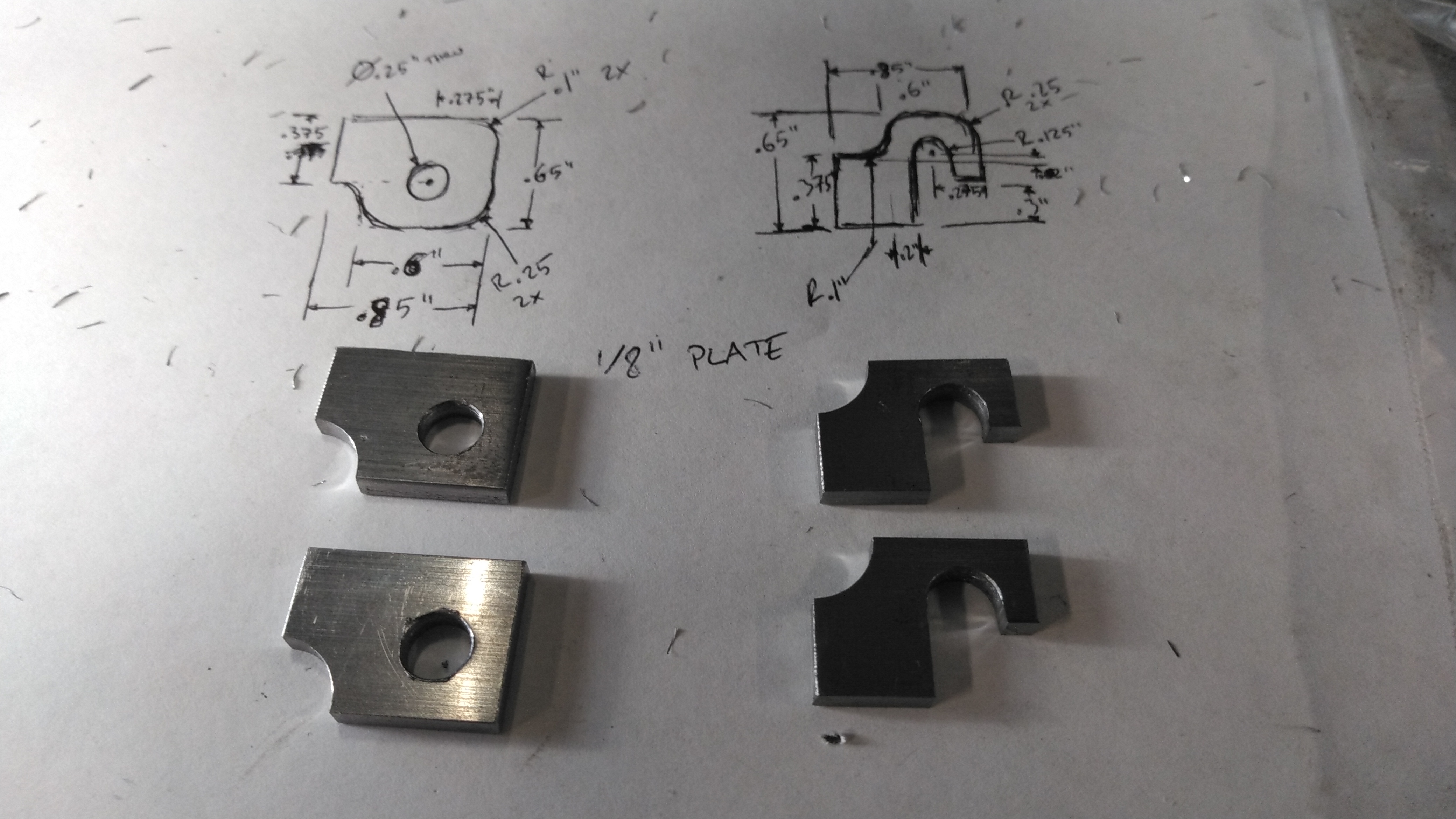 four steel hinge components laid out on top of a drawing